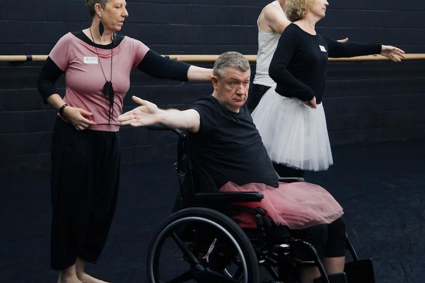 A man in a wheelchair with an outstretched arm wearing a pink tutu 